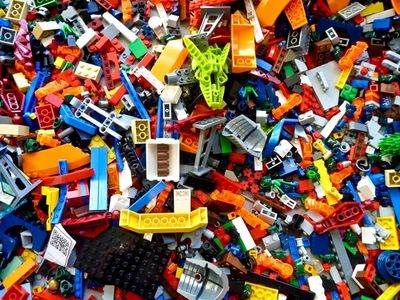 Many Lego pieces of various shapes and colors are scattered in chaos on a flat surface..jpg
