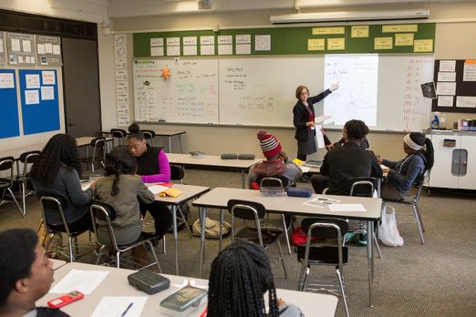 Photo-of-teacher-at-board-in-classroom-full-of-students.jpg