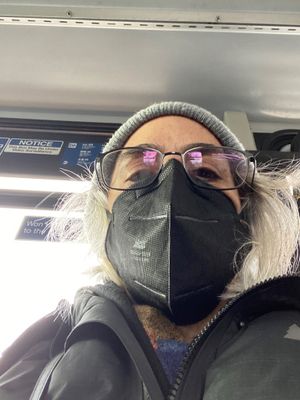 A selfie of Susan as the Masked Commuter, posing on public transit in a black mask and winter clothes..jpg