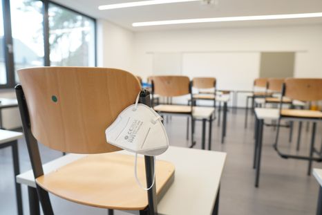 an empty classroom with a mask hanging from one of the chairs.jpg