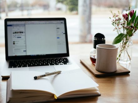 notebook, pen, MacBook, mug, vase with flowers on wooden table.jpg