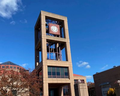 Cheney-Goodman-Schwerner Clock Tower under a bright blue autumn sky with trees and college buildings in the background.