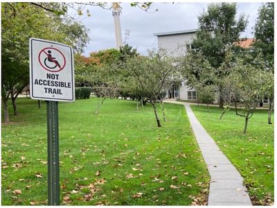 Sign on campus lawn near a classroom building that reads “Not Accessible Trail”