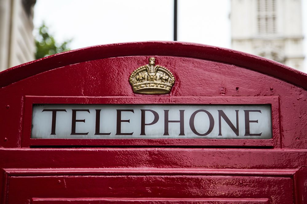 A photo of the top of a British red telephone box, focused on the word &quot;TELEPHONE&quot; and a royal crown decoration.